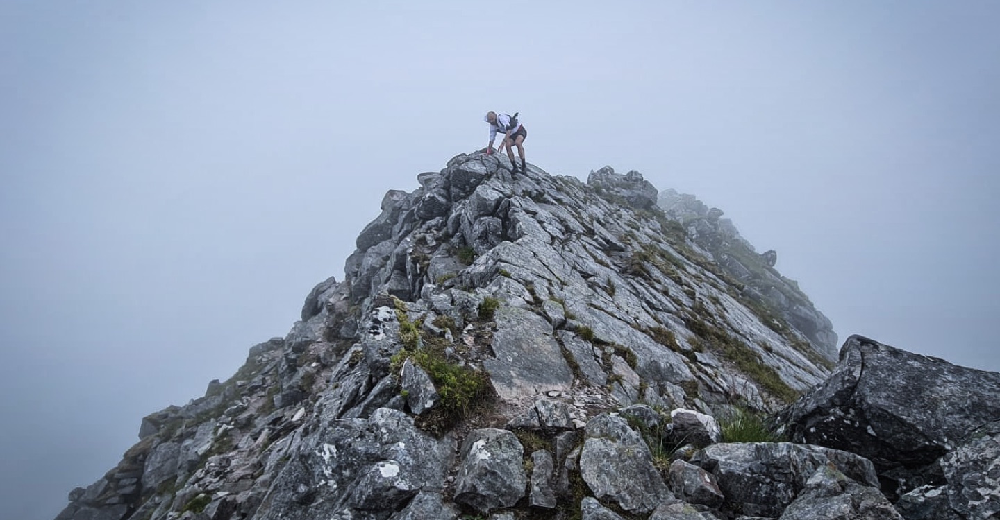 Pete feels his way over a knife edge rocky ridge in Scotland, on a cloudy day.
