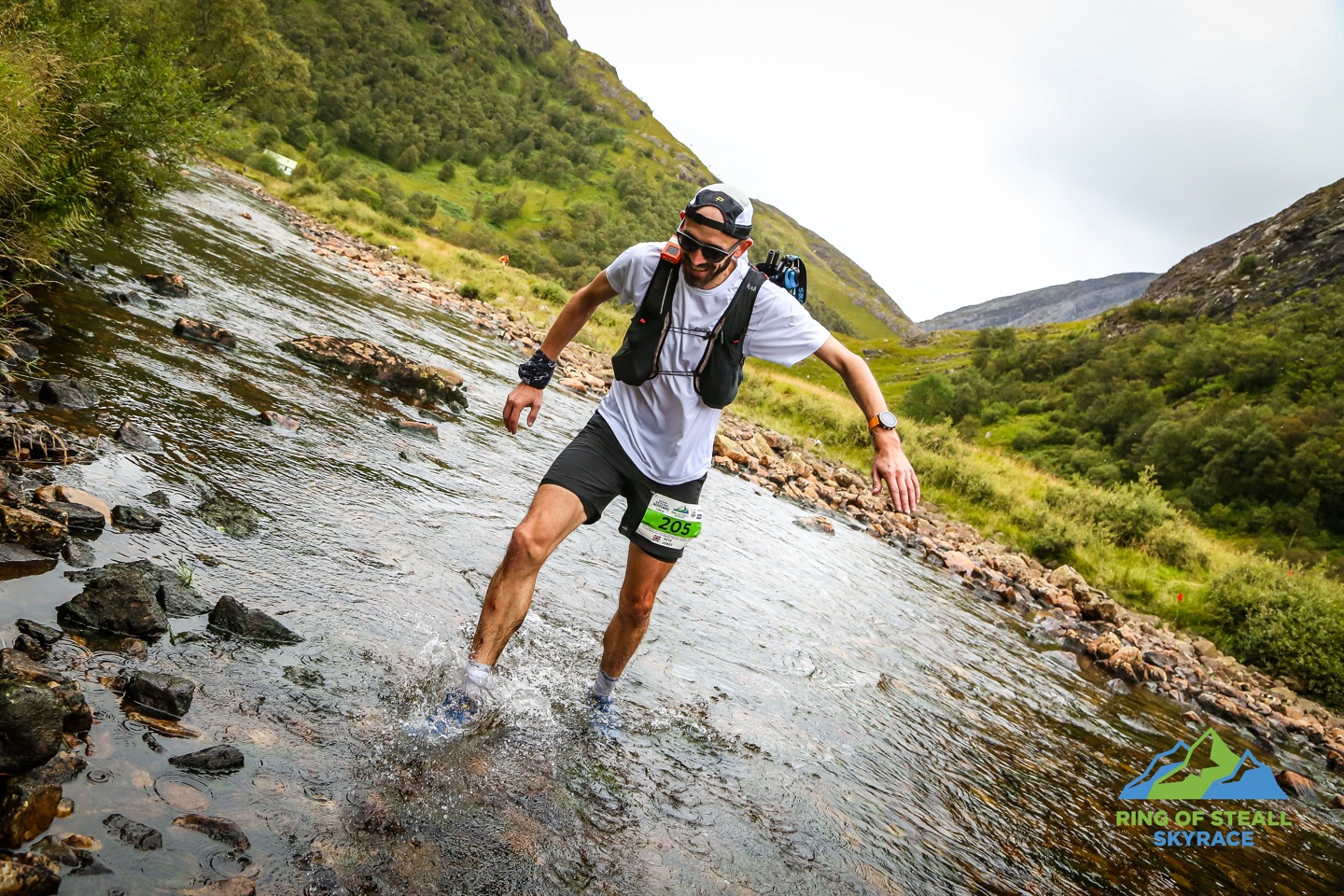 Pete crossing a river in Glen Nevis with a view of a green valley behind him