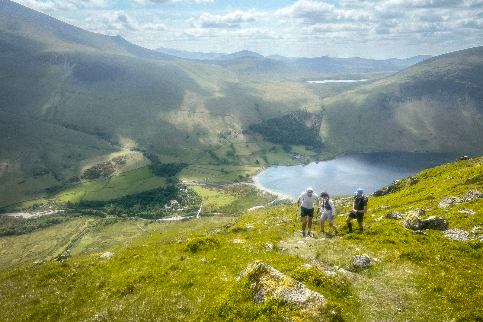 Pete climbing up Yewbarrow from Wasdale, using trail running poles. He is supported by two support runners. It is a sunny day and the lake is visible in the background.