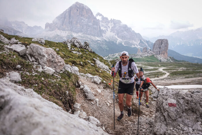 A runner climbs up a rocky trail with a big mountain behind.
