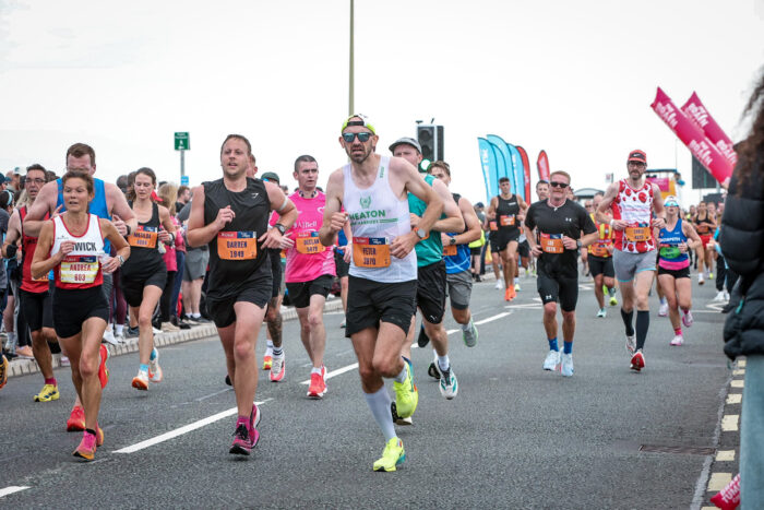 The author is central to a group of runners running along the road. He is in a white vest and fluorescent nike shoes, looking visibly strained.