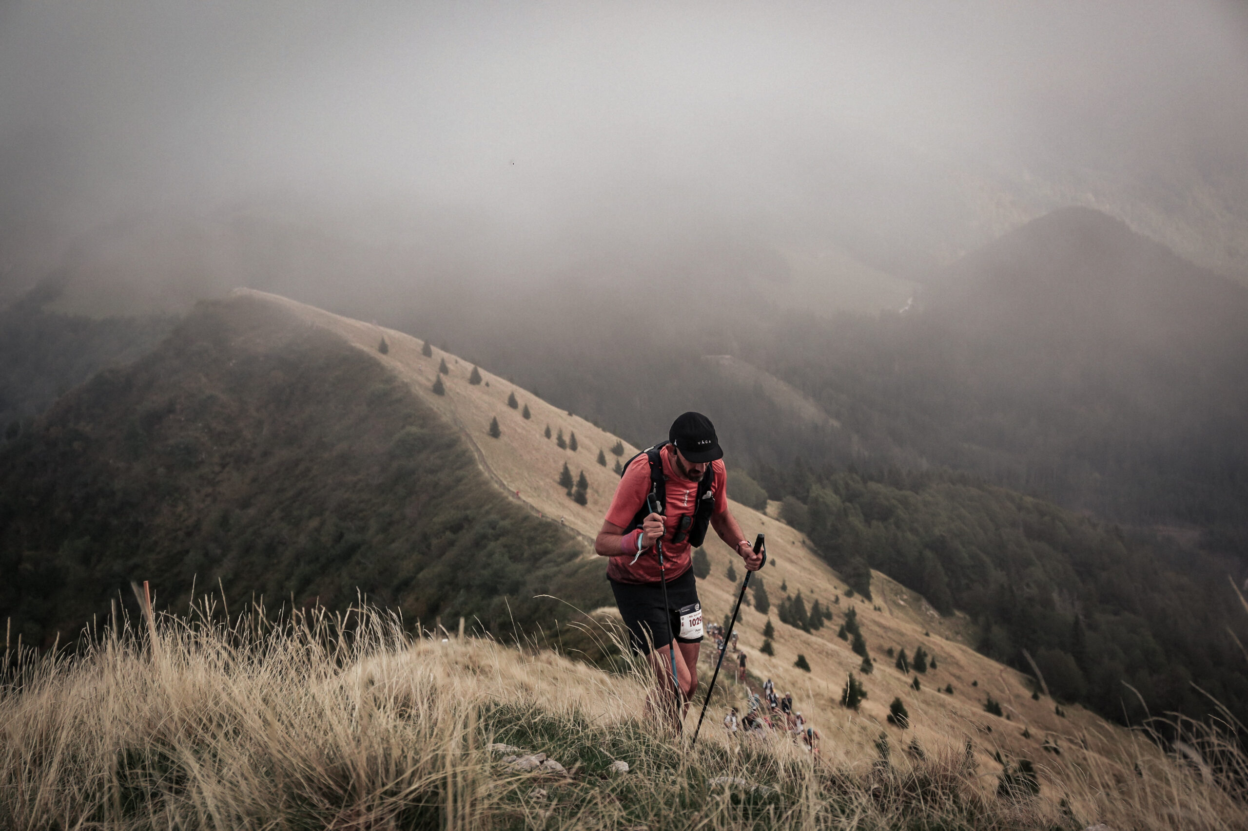 A trail runner runs along a ridge line with misty mountains in the background.